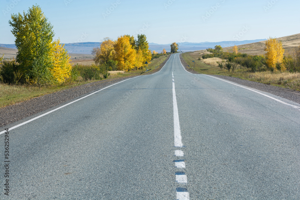 The asphalt road runs through the steppe and goes far into the mountains. Autumn The asphalt road runs through the steppe and goes far into the mountains. Autumn