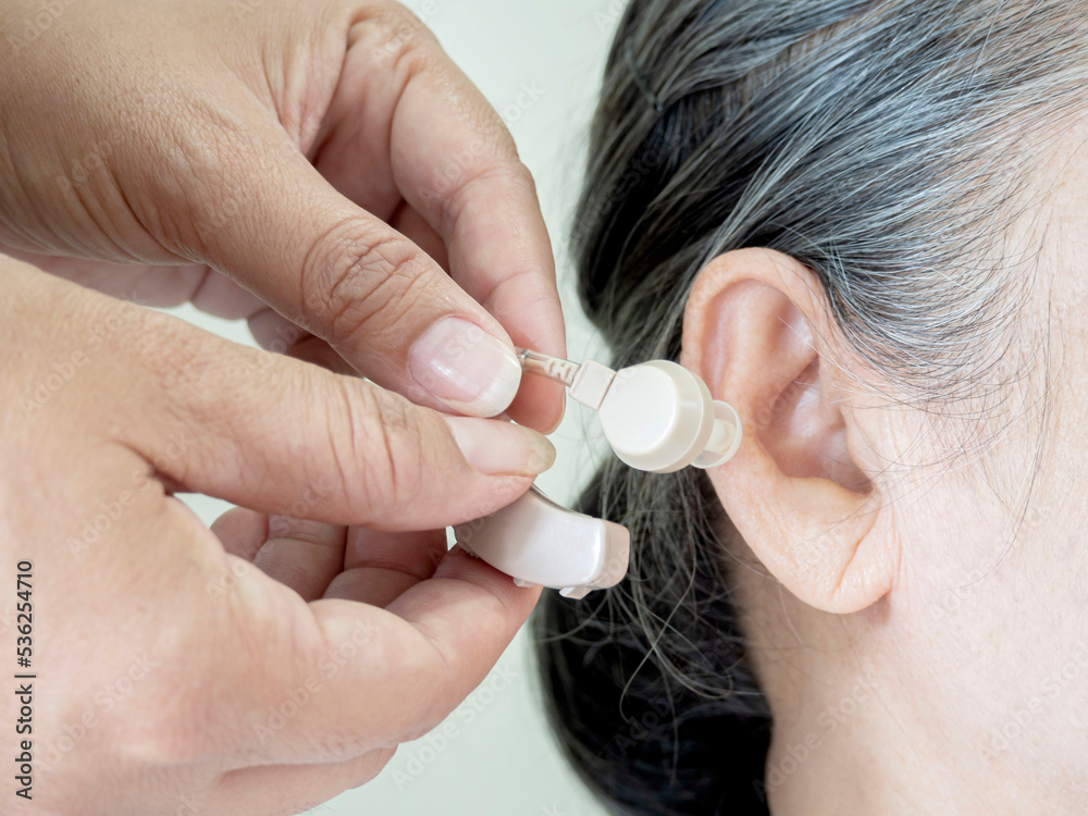 Fototapeta premium Close up of hands put the hearing aid on the senior woman ear.