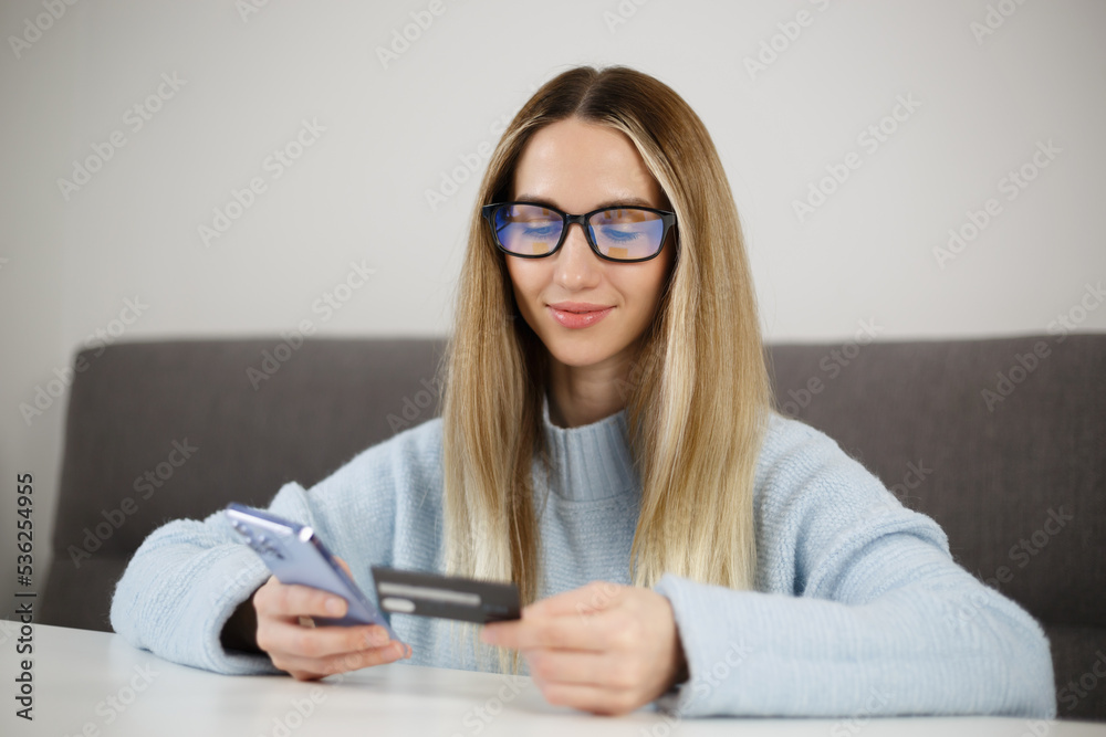 White woman paying online with credit card and mobile app in smartphone. Cheerful blonde female person makes money transfer in application White woman paying online with credit card and mobile app in smartphone. Cheerful blonde female person makes money transfer in application