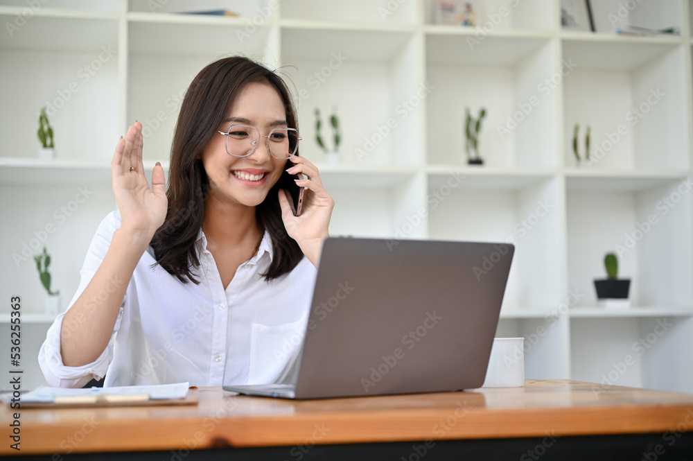 Charming Asian businesswoman having a good conversation with her client on the phone