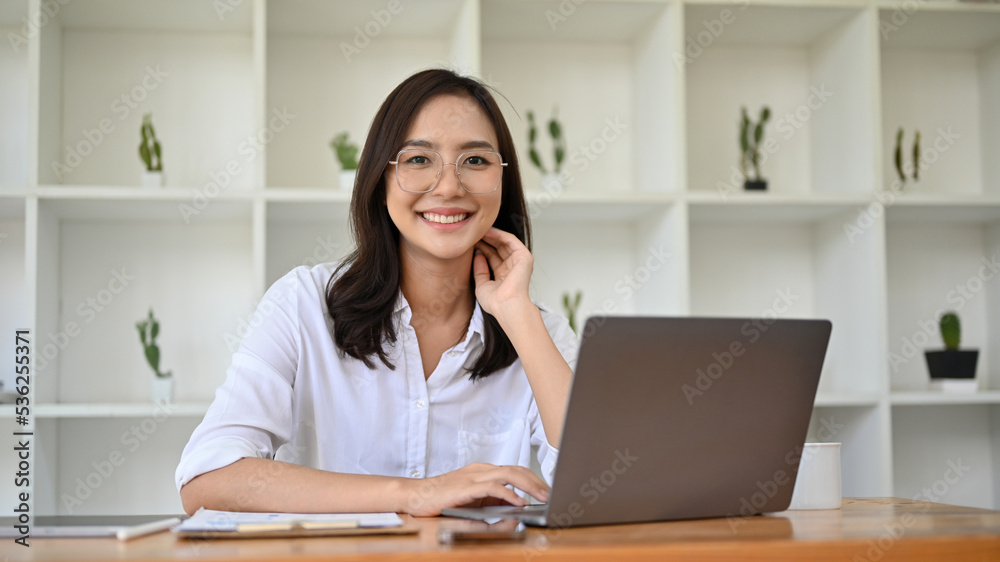 Attractive Asian businesswoman sitting at her office desk, smiling and looking at camera. Attractive Asian businesswoman sitting at her office desk, smiling and looking at camera.
