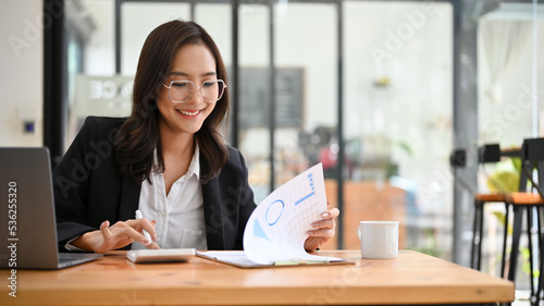 Positive Asian businesswoman working, using calculator to recheck a financial report. © bongkarn