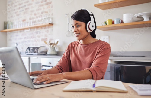 Email, music and black woman typing on the internet on a laptop while working at a table in her house. Remote African worker planning on web with technology while listening to a podcast in her home