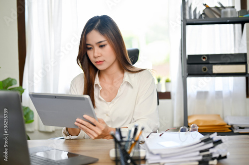 Successful Asian businesswoman at her desk, using tablet to recheck her financial data.