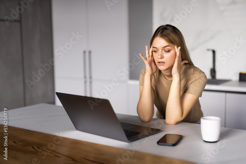 Sad upset freelancer touching temples laptop near cup of coffee on table