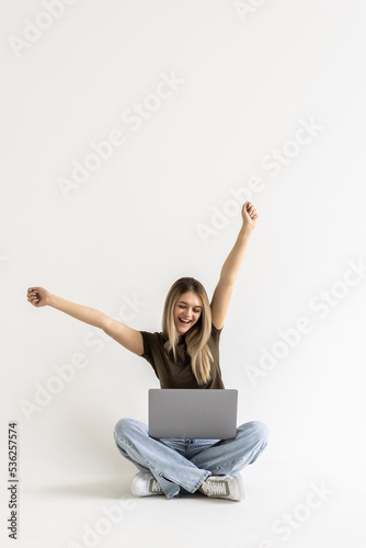 Young woman sitting with laptop with win gesture on white background © dianagrytsku