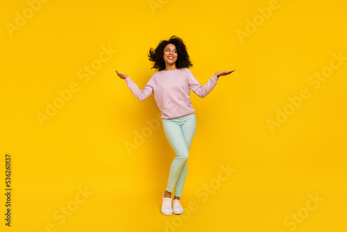 Full length photo of young cheerful girl standing guess look empty space isolated over yellow color background photo