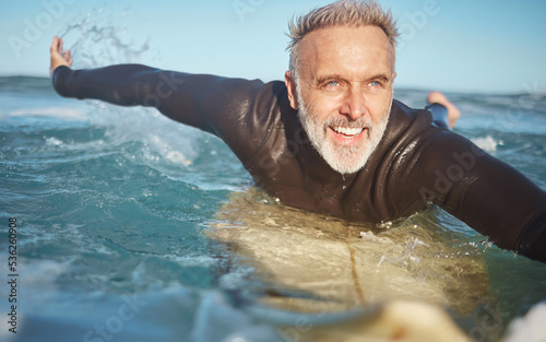 Beach, water and old man surfer swimming on a summer holiday vacation in retirement with freedom in Bali. Smile, ocean and senior surfing or body boarding enjoying a healthy exercise on sea of Island