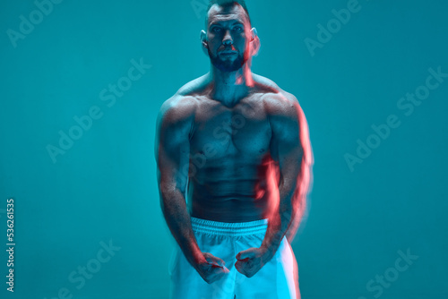 Muscular athletic man with naked torso showing his trained muscles in neon studio light. Long exposure. Copy space