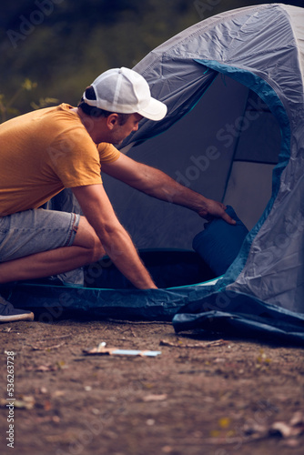 Man camping in nature, setting up the tent for overnight staying near forest river.