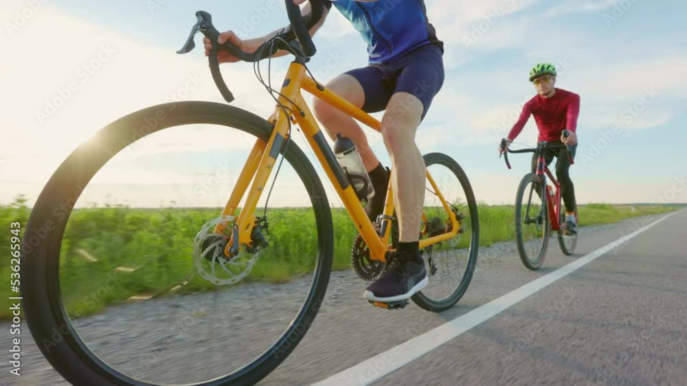 Two cyclists in sportswear riding their bikes on asphalt road. Professional athletes wearing safety helmets, sport clothes and glasses. Outdoors activity concept. Two cyclists in sportswear riding their bikes on asphalt road. Professional athletes wearing safety helmets, sport clothes and glasses. Outdoors activity concept.