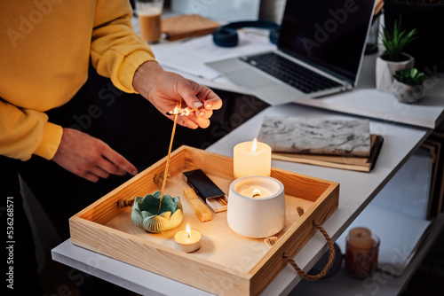 Meditation  relaxation after work. Woman getting ready meditating and lights up indian incense stick and candles. Woman hands with Smoke indian incense stick  burning candles on the table at home