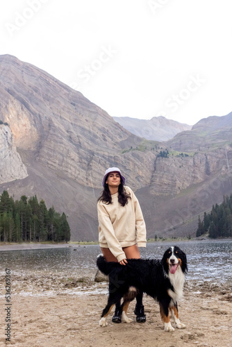 brunette girl with white cap and jacket posing on the mountain with a cute dog photo