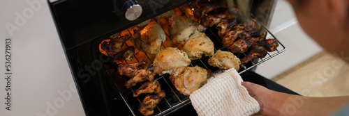 Woman cook taking out baked chicken from oven on baking sheet closeup