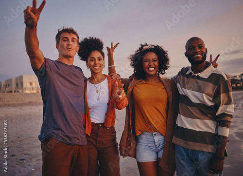 Diversity, friends and on beach at sunset show peace, sign or relax together on holiday and vacation. Happy group, smile or on seaside getaway, trip or weekend break have fun, good time or travelling