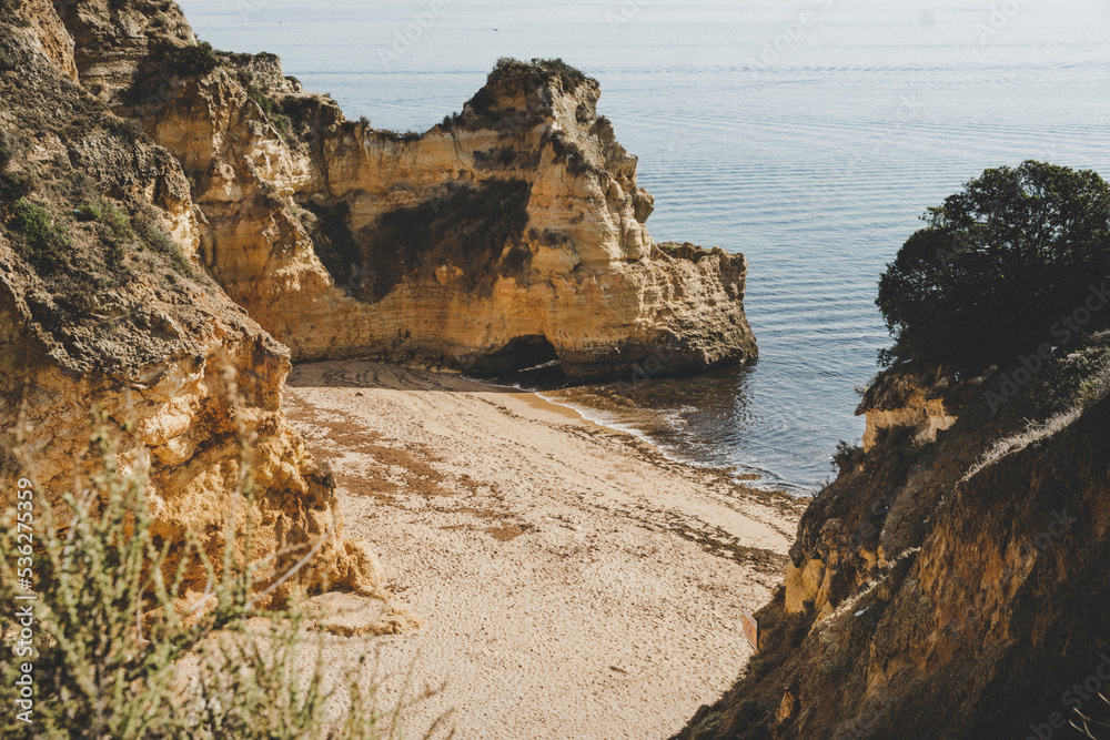 Fototapeta premium Empty and abandoned beach surrounded by cliffs on the coast of Algarve near Lagos.