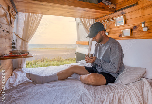 Photos Hombre joven caucásico, en la cama de la camper, desayunando, relajado