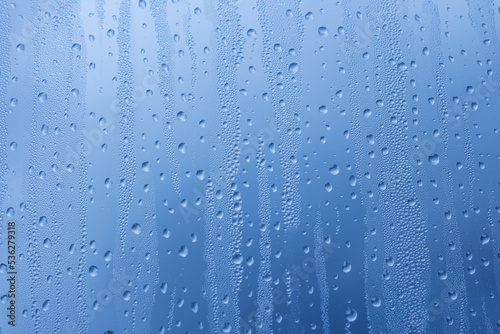 Close-up of raindrops on a window pane. Gloomy wet weather. Drops of water on glass in front of dark blue rain clouds. Rain. Abstract background texture. Wallpaper.