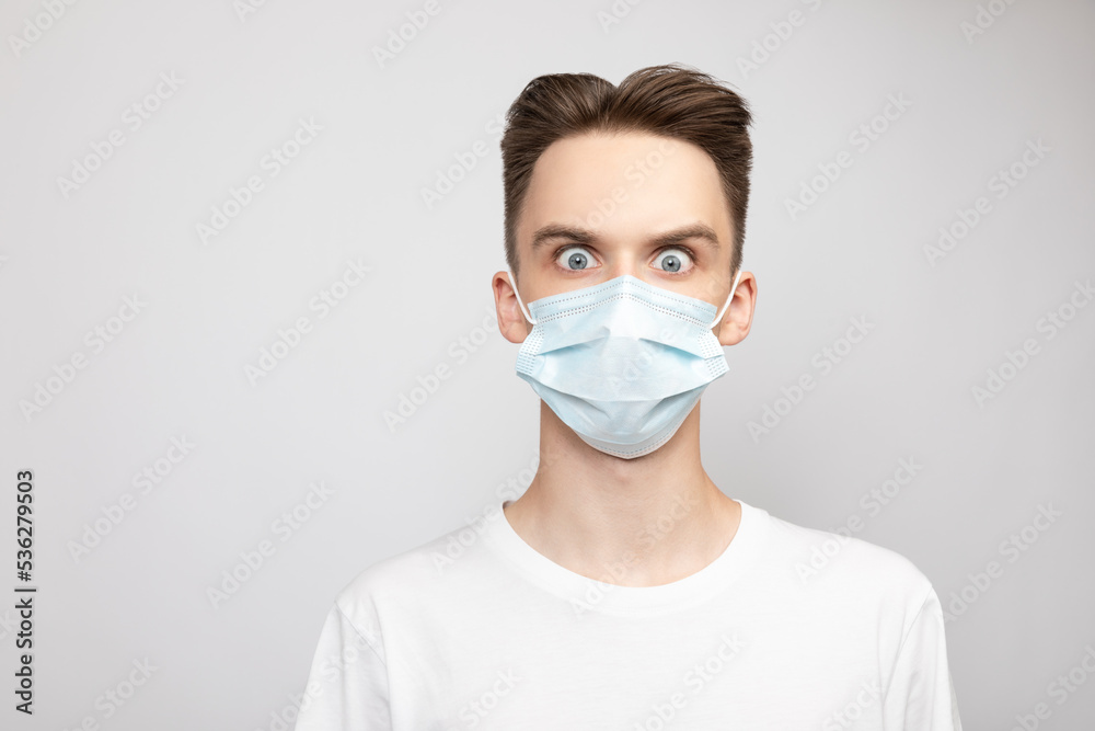 Young man wearing medical mask with eyes wide open studio shot on gray background Young man wearing medical mask with eyes wide open studio shot on gray background