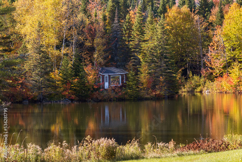Tiny cabin nestled in colourful fall foliage at the edge of a small lake, Stoneham-et-Tewkesbury, Quebec, Canada