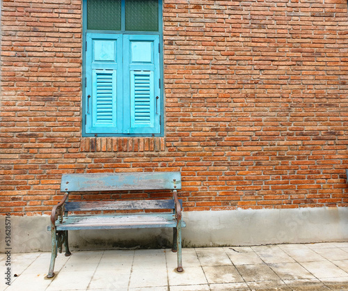 old wooden long bench armchair on concrete floor in front of old red brick wall and ancient wooden fresh blue windows