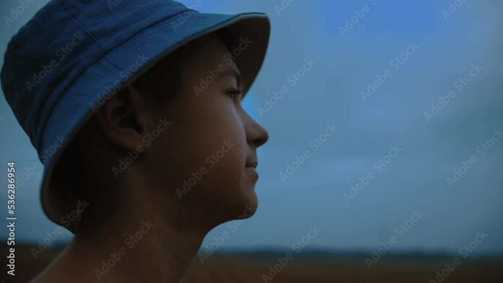 profile of a happy boy in a hat against the backdrop of a blue rainy sky, moving camera profile of a happy boy in a hat against the backdrop of a blue rainy sky, moving camera