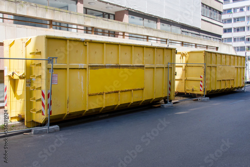 Yellow garbage containers near the building, construction site on the background. Recycling, construction waste, dumpster near construction site.