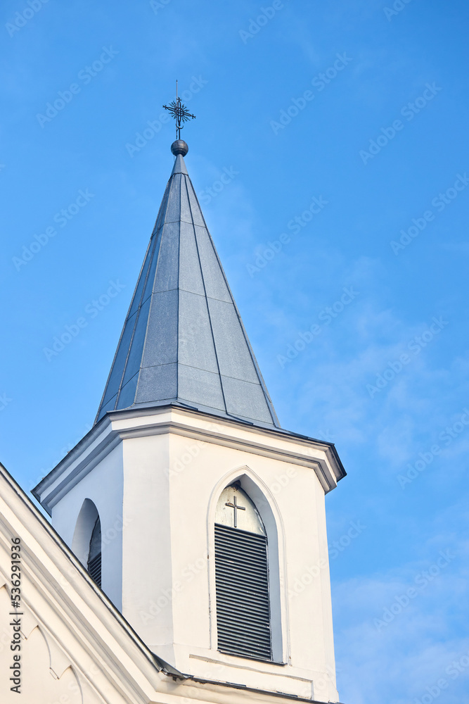 White church steeple with cross with window blind and cross over blue sky background with copyspace.