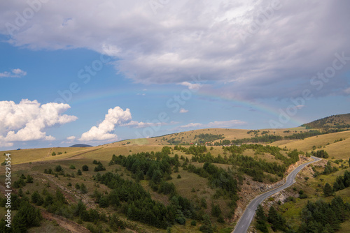 Aerial view of golden pine forest at Zlatibor mountain in Serbia, with rainbow in background. Shot from gondola or cable car. Scenic view of Zlatibor mountain.