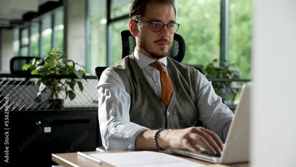 Businessman working on laptop computer at office. Male professional typing on laptop keyboard at workplace. Portrait of positive business man looking at laptop screen indoors Businessman working on laptop computer at office. Male professional typing on laptop keyboard at workplace. Portrait of positive business man looking at laptop screen indoors