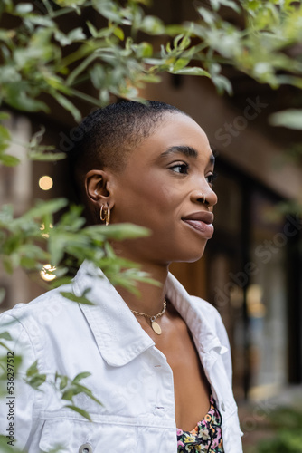 Portrait of stylish african american woman standing near blurred tree outdoors.