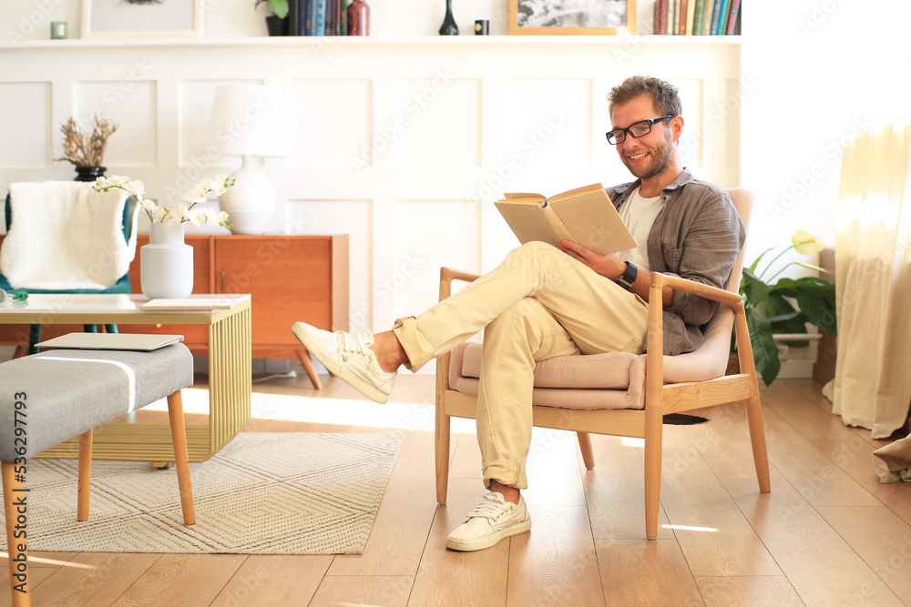 Young man is reading a book sitting in a chair at home