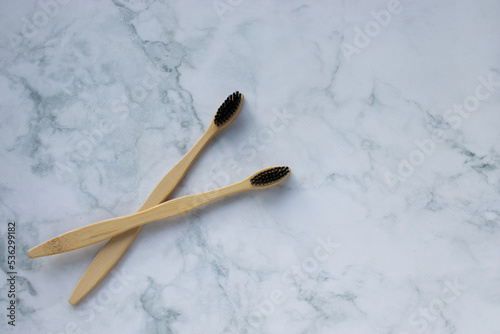 Natural bamboo toothbrush with black bristles on white marble table in bathroom. View from above. Zero waste, reusable, sustainable, eco friendly tooth brush