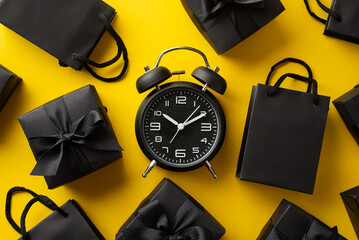 Black friday shopping concept. Top view photo of black alarm clock paper bags and gift boxes with ribbon bows on isolated yellow background