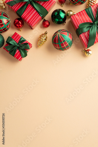 New Year concept. Top view vertical photo of present boxes with ribbon bows green red baubles and gold pine cone ornaments on isolated beige background with copyspace