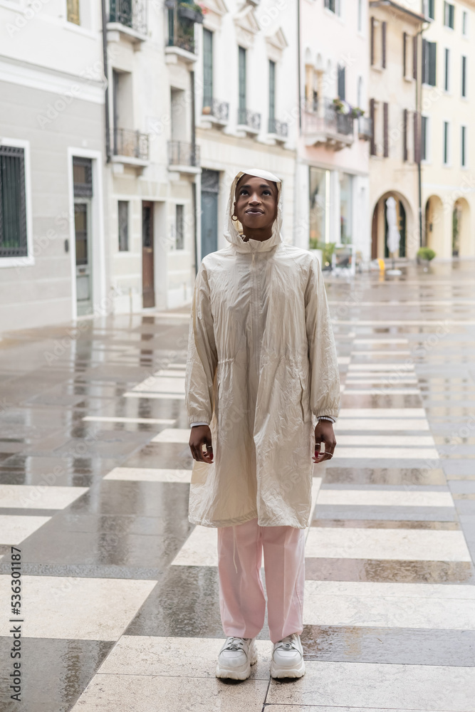 Fashionable african american woman in raincoat standing on blurred street in Italy.
