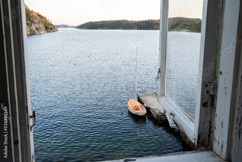 Old open window through which view of sea, a rocky coast, a moored sealing boat and sky at sunset.  photo