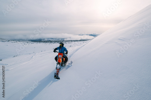 Snowbike rider riding on steep snowy slope. Modify motorcycle with ski and special snowmobile-style track instead of wheels