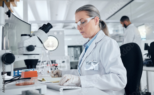 Laboratory, microscope and woman typing on computer for medical data, petri dish test results or healthcare cancer research. Mature scientist, worker or dna science engineer in Sweden with technology
