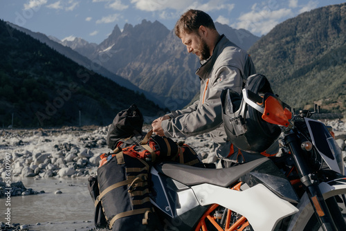 man attaching padded saddlebags for off-road motorcycle to the trunk in beautiful mountain gorge