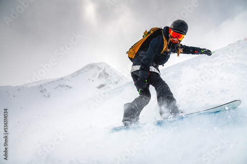 snowboarder quickly descends creating a wave of snow against the backdrop of mountains. ski resort. off-piste, free-riding