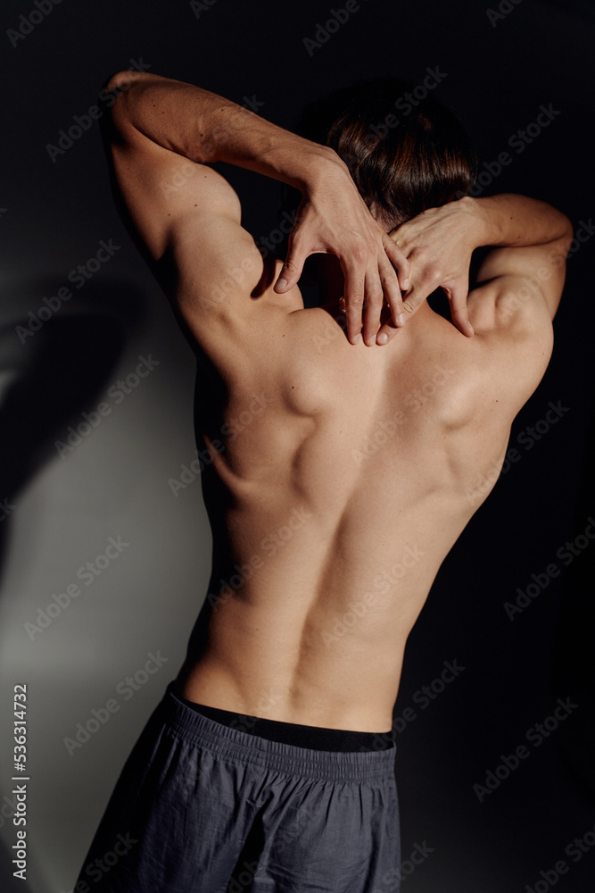 back view of muscular shirtless man posing on black and grey background.