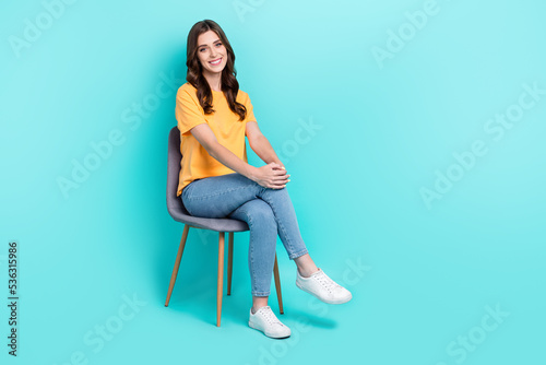 Full length photo of sweet pretty girl dressed yellow t-shirt smiling sitting chair empty space isolated teal color background © deagreez