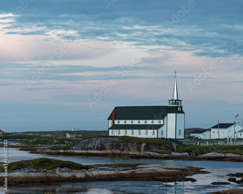 Historic St. Luke’s Anglican Church, Newtown, Newfoundland and Labrador, Canada. A white located on a rocky shoreline with clouds and late evening light.