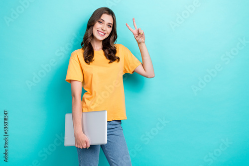 Photo of young attractive cute nice pretty woman wear orange t-shirt hold laptop showing v-sign empty space ad app for dating isolated on cyan color background