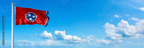 Tennessee, - state of USA, flag waving on a blue sky in beautiful clouds - Horizontal banner
