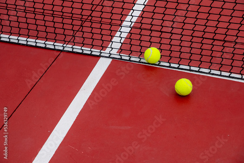 two tennis balls at the net of a red court