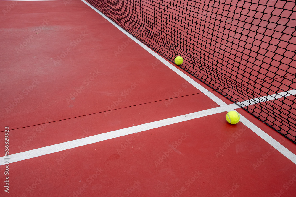 two tennis balls by the net of a red court