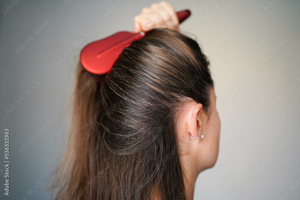 Naklejka premium A woman combs her hair. Gray hairs on the head of a young girl. Long gray hair. The initial stage of gray hair. The problem of gray hair in women.