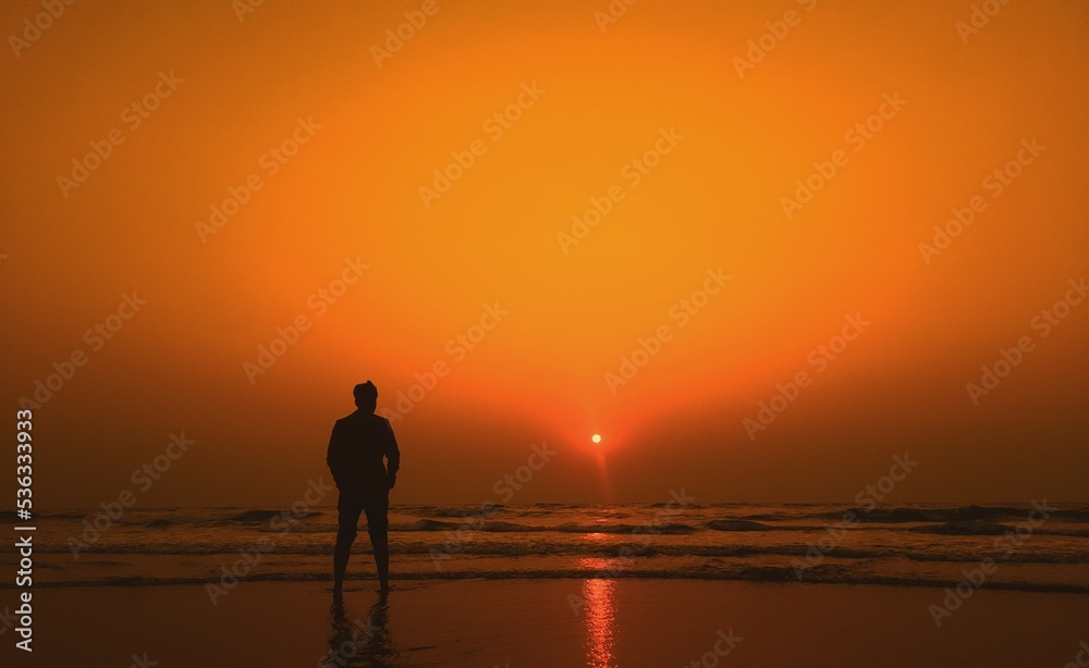 The silhouette of a young man admires the sunset on the sea. healthy lifestyle. freedom, inspiration, Nature, and beauty concept. Orange sundown.	